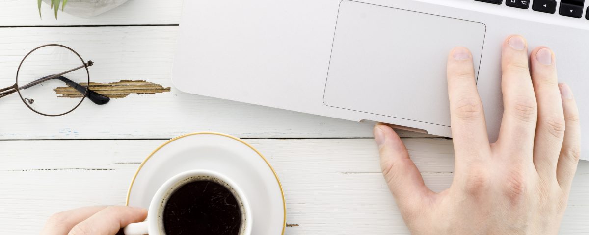 Una pantalla con una web moderna abierta, y una mano tomando notas con una taza de café al lado.